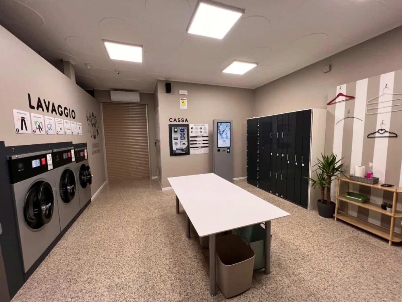 Un Lavasecco Point dentro una lavanderia self service: lavatrici a gettone, totem e armadietti
