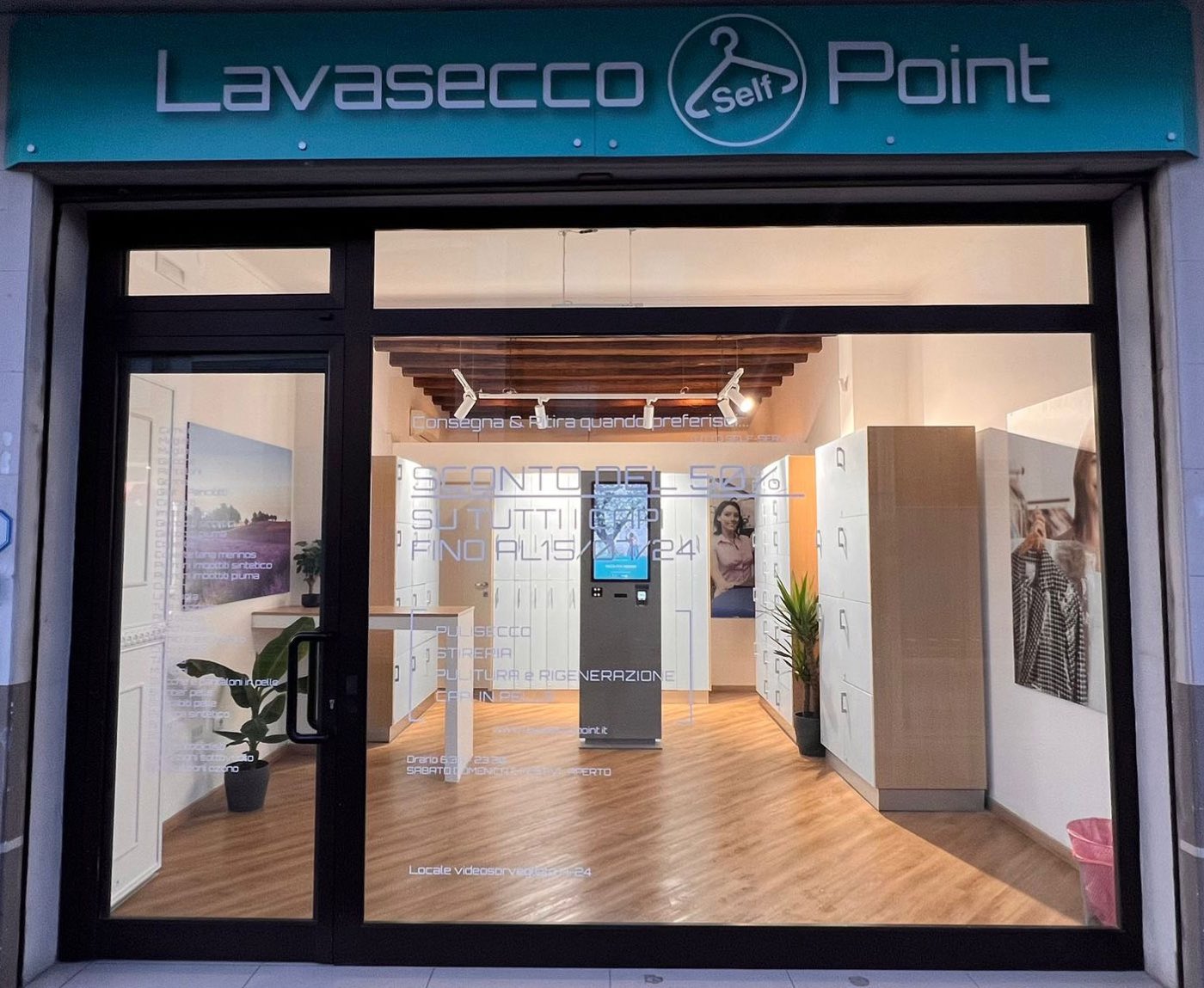 Vetrina di un Lavasecco Point: insegna verde acqua, totem e armadietti bianchi